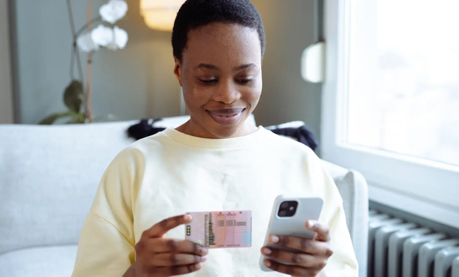 An image of a woman looking down at her mobile phone. She is holding her phone in one hand and her driving licence in the other.