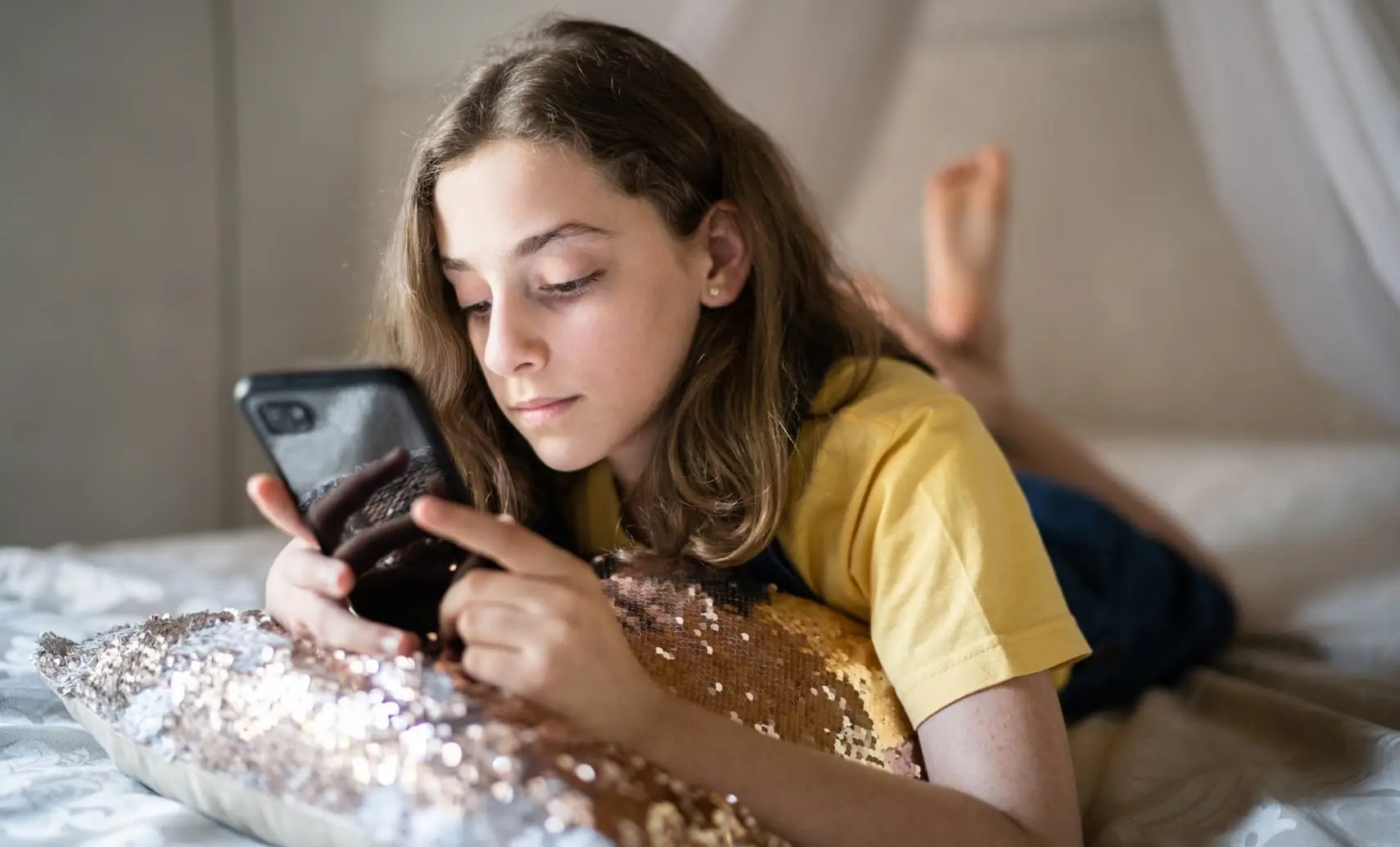 An image of a young girl who is lying on her bed and using a smartphone.