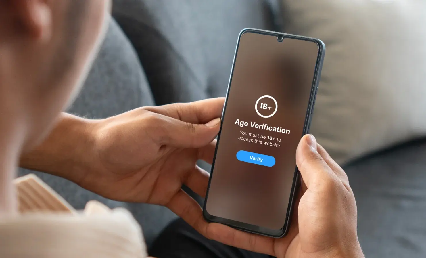 Why am I being asked to prove my age online? An image of someone holding their mobile phone. On the screen, the platform is asking for the user to verify their age to access age-restricted content.